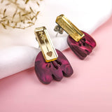 Introducing the Romantic Tulip Earrings—a pair of earrings with gold rectangular tops and dangling marbled purple acrylic shapes, featuring a small gold chain and heart charm. Allergy-free and stylish, they rest on white fabric with dried flowers on a pink background.
