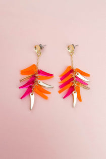 Gold dangle earrings with dangling pink, orange, and gold leaf-shaped charms arranged in layers, these featherlight earrings are displayed on a pale pink background.