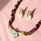 A handmade necklace and matching clip-on earrings with white, acrylic tulip-shaped pendants, gold accents, and a fabric-wrapped brown and pink chain, displayed on a soft pink background.